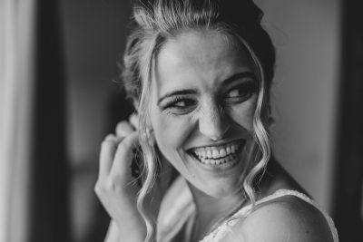 Braut steckt Ohrringe an und lächelt glücklich – emotionaler Moment während der Hochzeitsvorbereitungen.