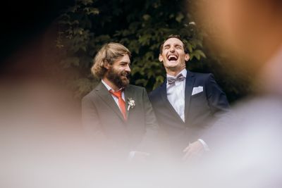 Zwei lachende Männer im Anzug bei einer Hochzeit im Freien – festlicher Moment mit Freude und Freundschaft.