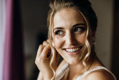 Nahaufnahme der Braut, die sich lächelnd vorbereitet und Ohrringe anlegt – natürliche Hochzeitsstimmung.