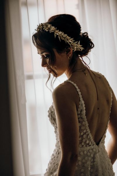 Porträt der Braut im Gegenlicht am Fenster, elegantes Spitzenkleid mit Blumenkranz.