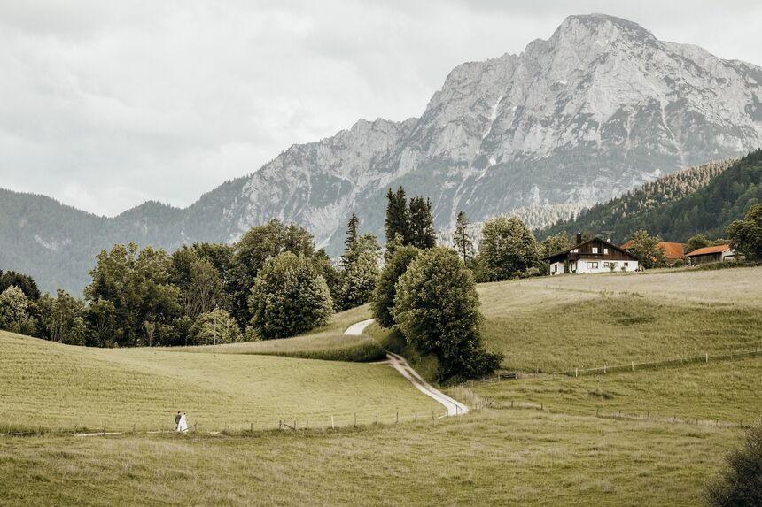 Braut und Bräutigam spazieren über eine Wiese vor beeindruckender Bergkulisse – romantische Hochzeitsaufnahme in der Natur.