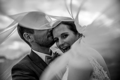 Fröhliches Brautpaar unter dem Schleier – emotionales Schwarz-Weiß-Foto voller Nähe.