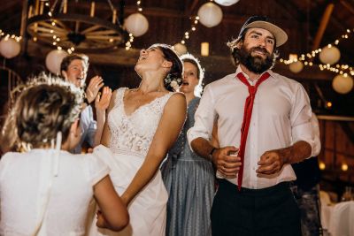 Fröhliche Gesellschaft auf der Hochzeitsparty mit Braut in Spitzenkleid und Gästen, die gemeinsam tanzen und feiern.