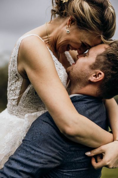 Bräutigam hebt Braut in den Armen, beide lächeln sich liebevoll an – romantisches Hochzeitsfoto.