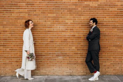 Braut und Bräutigam lachen sich an vor einer Backsteinwand – urbanes Hochzeitsfoto.