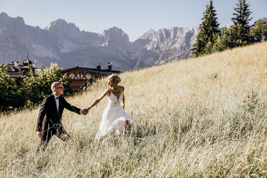 Braut und Bräutigam halten sich an den Händen auf einem Feld unter blauem Himmel – romantischer Moment.