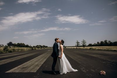 Braut und Bräutigam küssen sich auf einer Landebahn unter blauem Himmel – modernes Hochzeitsfoto.