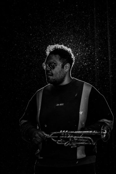 Musiker in dunklem Licht mit Trompete in der Hand – künstlerisches Porträt in Schwarz-Weiß.