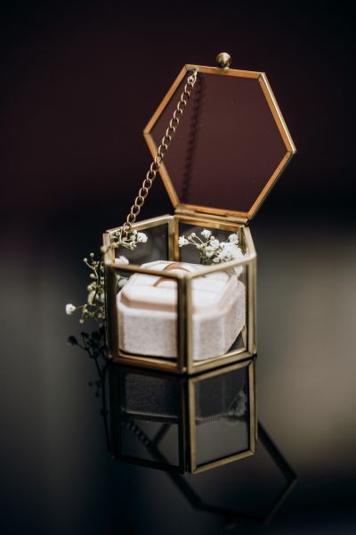Goldene Eheringe in edler Glasbox mit Blumenarrangement – elegantes Hochzeitsdetailfoto.