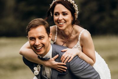 Bräutigam trägt seine lachende Braut auf dem Rücken – authentischer Hochzeitsmoment.